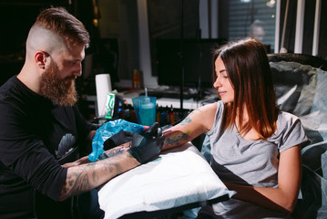 Professional tattoo artist makes a tattoo on a young girl's hand.