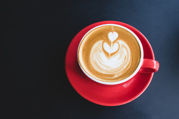 A cup of coffee with latte art in red cup on black table