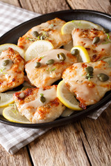 Plate with chicken piccata on wooden board closeup. Vertical