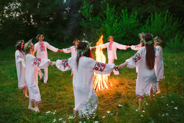 Midsummer. Young people in Slavic clothes circle dance around a bonfire in the forest. - obrazy, fototapety, plakaty