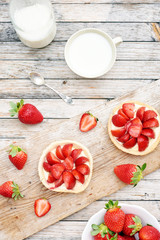 Vertical top view of strawberry tarts, fresh milk and strawberry in a bowl on rustic wooden table. 