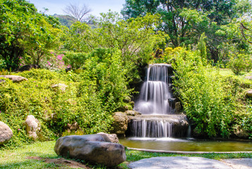 Small waterfall in the spring garden among green tropical plants photo