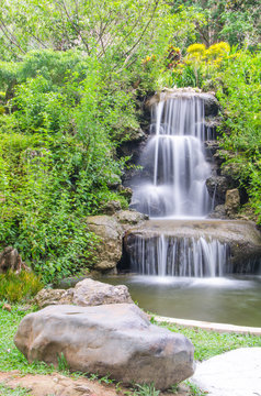 Small waterfall in the spring garden among green tropical plants photo