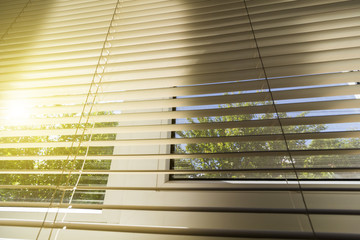 The summer sun shines through the blinds of the window of a rural house.