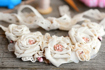 Cute shabby chic necklace on a vintage wooden background. Female flower necklace made of cotton fabric, lace ribbons and beads. Simple way to turn old cloth into jewelry. Closeup