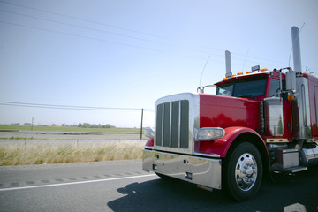 Gorgeous bright red shiny big rig semi truck with chrome parts and accents driving separated lines road