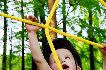 Fototapeta premium Little boy is very concentrating on climbing in the natural rope park in the wood.