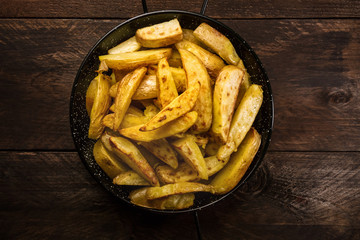 Crunchy roasted potatoes in skillet on dark rustic texture