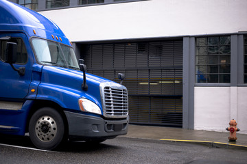 Modern shiny blue semi truck driving with cargo by urban city street