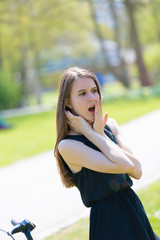 A girl in a summer park is surprised and laughs covering her mouth with her palm