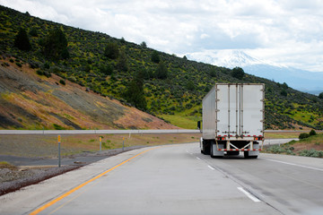 Semi truck with semi trailer move down on winding highway with green hills