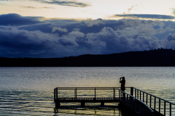 Silhouette young woman using mobile phone taking picture of beautiful Lake Taupo in the evening , North Island of New Zealand