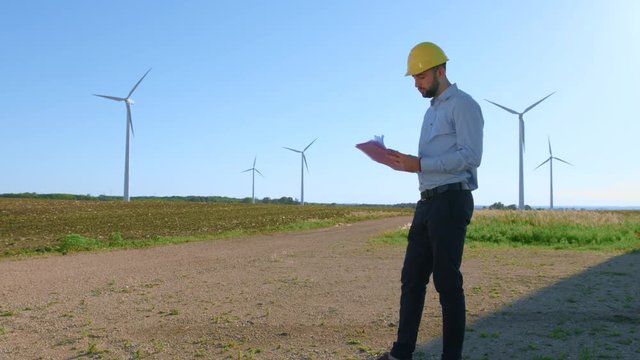 The engineer works with the drawings against the background of windmills