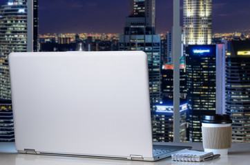 Laptop on table in office with panoramic night view of modern downtown skyscrapers at business district