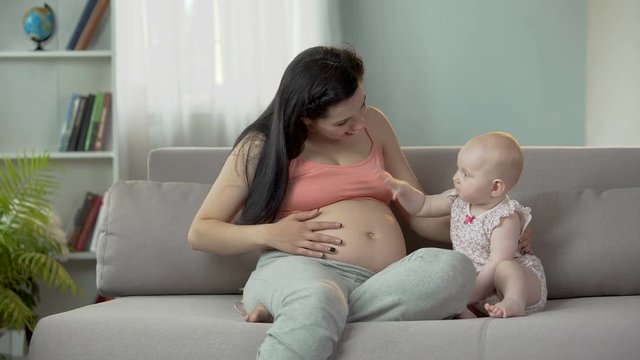Playful sweet baby girl clapping pregnant mother on big belly, happy maternity