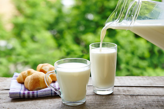 Milk from a glass jug poured into a glass. Croissants breakfast in nature