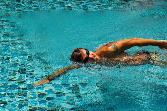 Young man is swimming in a transparent water of a pool in a sunny day.