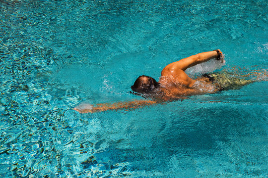 Young man is swimming in a transparent pure water of a pool in a sunny day.