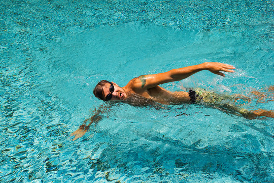 Young man is swimming in a transparent pure water of a pool in a sunny day.