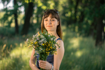 Beautiful girl with a bouquet of wildflowers in the nature.