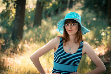 Happy young girl in a hat walks in the park in the summer day.