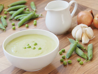 Vegetable pea soup and ingredients for cooking. Peas, cream, onion and garlic. Wooden background. Close up view.