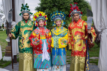 Fototapeta na wymiar group of four asian people men and women standing in a row and greeting outdoor in traditional chinese costumes
