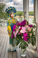 Fototapeta na wymiar beautiful chinese girl in traditional chinese dress and pompon hat standing near the big peony and orchid bouquet