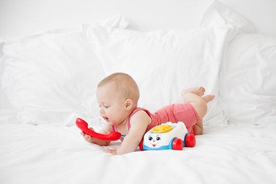 baby lying on a bed talking to a toy phone