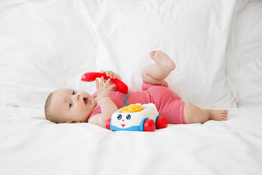 cute baby lying on a white bed playing with a toy phone