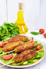 Lula-kebab is a meat dish, traditional for the Caucasus, in Central Asia and Turkey. Minced meat strung on a skewer and fried. Serve on a plate with lettuce leaves and fresh tomatoes. Vertical view