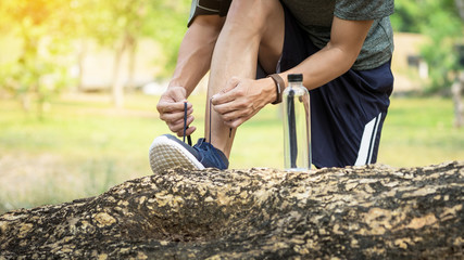 Cropped shot of young man runner tightening running shoe laces, getting ready for jogging exercise outdoors. Male jogger lacing his sneakers standing on forest path before morning run