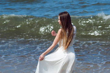 Fototapeta na wymiar Young charming brunette woman on sea coast. Beautiful girl in a white summer dress. Runs towards the sea, back view
