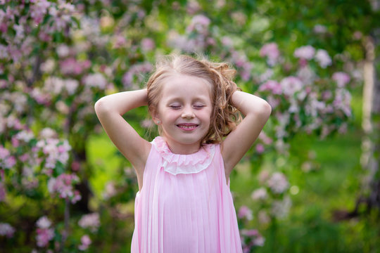Portrait of a happy little girl in a blooming summer park with closed eyes