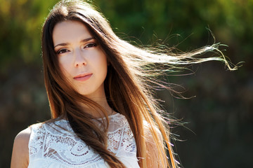 Young charming brunette woman. Closeup portrait outdoors on a background of green foliage.