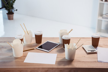 Close-up view of food boxes with chopsticks, disposable coffee cups and digital tablet on office table