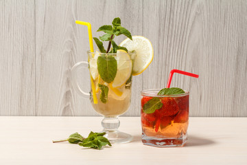 Cold  lemonade mojito with lemon and mint in a tall glass and strawberry lemonade with mint in a short one.on an wooden cutting board