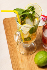 Cold  lemonade mojito with lemon and mint in a tall glass and strawberry lemonade with mint in a short one.on an wooden cutting board