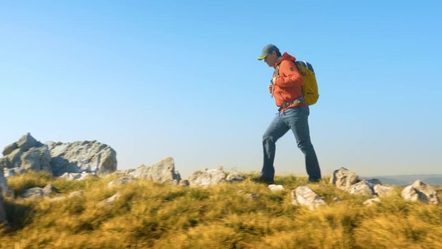 Low angle side tracking shot of a hiker walking on a rocky footpath.
