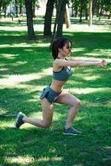 A sporty girl does a workout. Beautiful girl is training in summer in a green park. Sports mode.