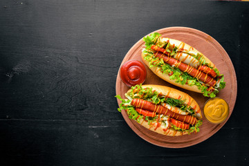 Hot dog with grilled sausage, mustard and ketchup, onions and greens on Wooden background. Top view. Free space.