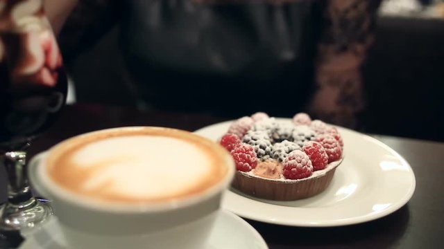 Woman eating dessert and drinking coffee in a cafe, close-up