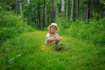 A girl in a hat with a bouquet of flowers on a forest path