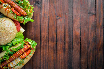 Hot dog and hamburger with cheese, meat and greens on Wooden background. Top view. Free space.