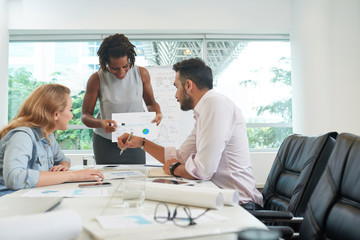 Friendly business coach conducting training course for sales managers in spacious boardroom, they sitting at table and listening to her with attention