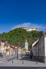 Rasnov, Romania - May, 2017: View of the Rasnov city mainstreet (Brasov county (Romania), with the hill of the medieval Rasnov fortress and city name in the Hollywood style
