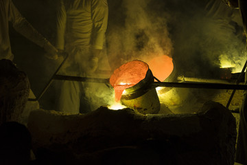 Foundry worker pouring hot molten metal into mold casting