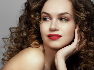 Brunette girl with long and shiny wavy hair . Beautiful model with curly hairstyle. Red lips