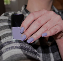 Frauenhand mit lila lackierten Fingernägeln hält Nagellackflasche 