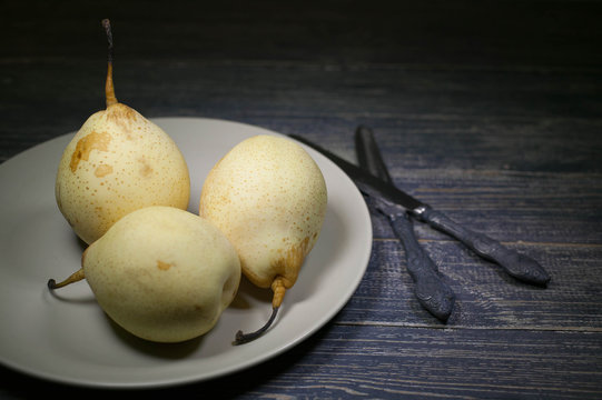 Fresh yellow Chinese pears and two knives on a dark wooden table. Selective focus. Food sweet background